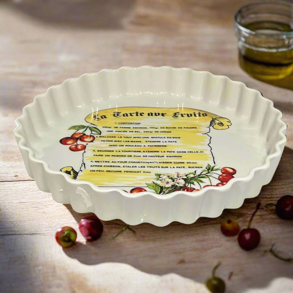 Decorative ceramic tart dish with recipe text and fruit illustrations on a table with cherries