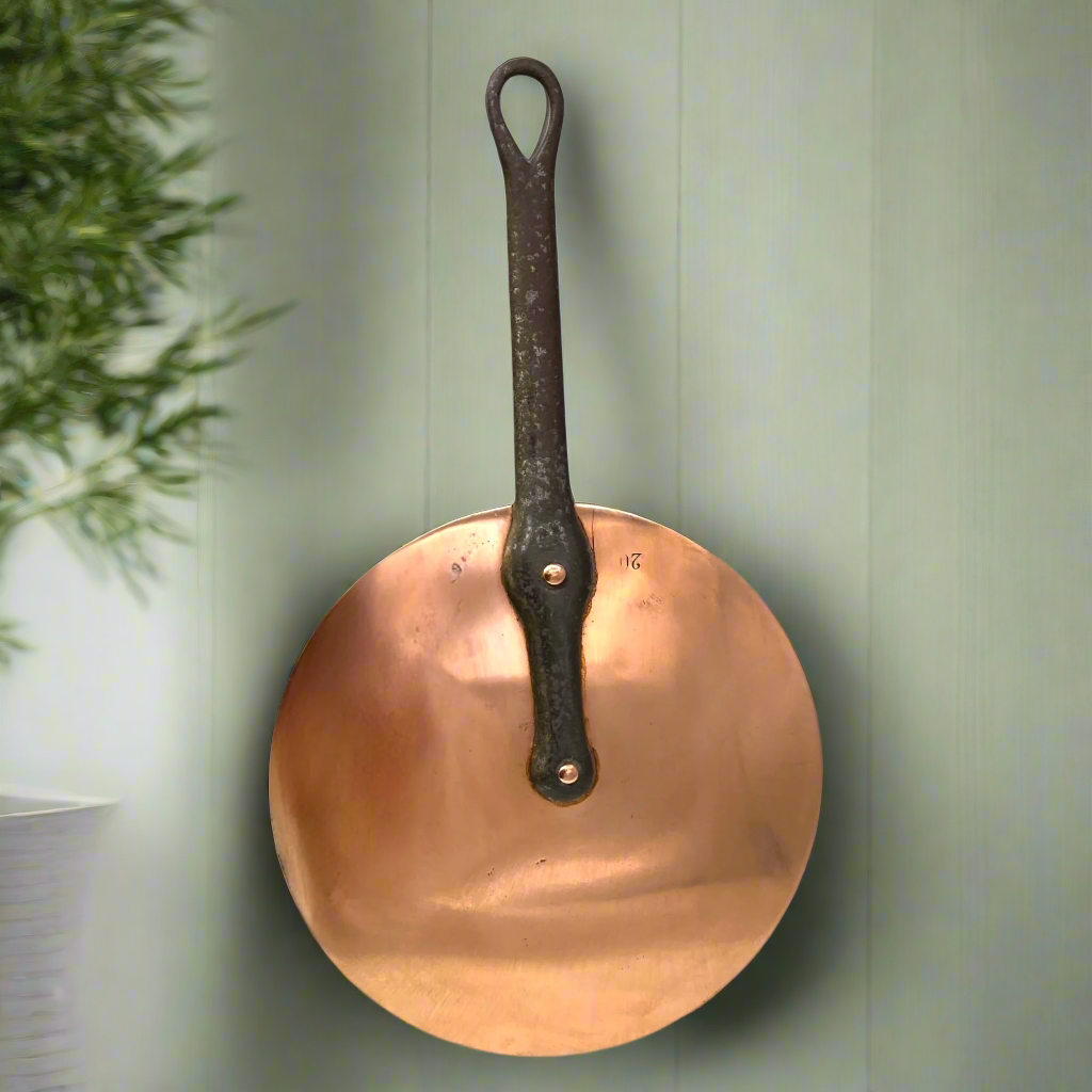 French vintage copper pan lid with a cast handle on a green wall beside a house plant