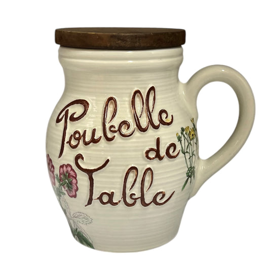 A cream-colored ceramic table jar with a dark wooden lid, featuring the French text 'Poubelle de Table' in brown script and pink floral illustrations shown on a white background