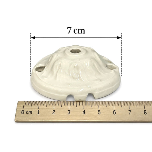 An off-white ceramic ceiling fan canopy with a 7 cm diameter, shown with a wooden ruler below for scale on a white background.