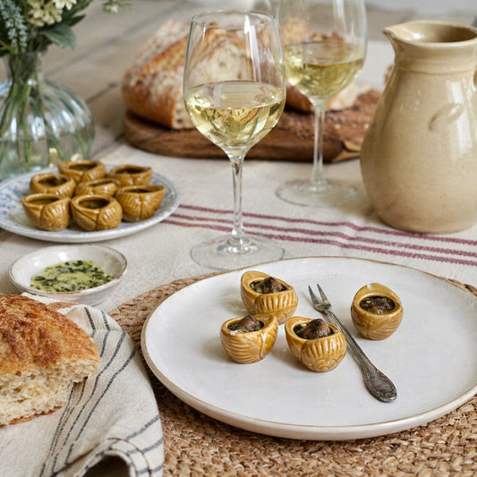Table setting with plates of small escargots appetizers, glasses of white wine, and bread.