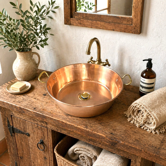 Copper up cycled sink basin with brass handles and a brass pop up waste, ideal for a rustic bathroom or camper van, set on a rustic wooden vanity unit with soap, a plant and a brass tap