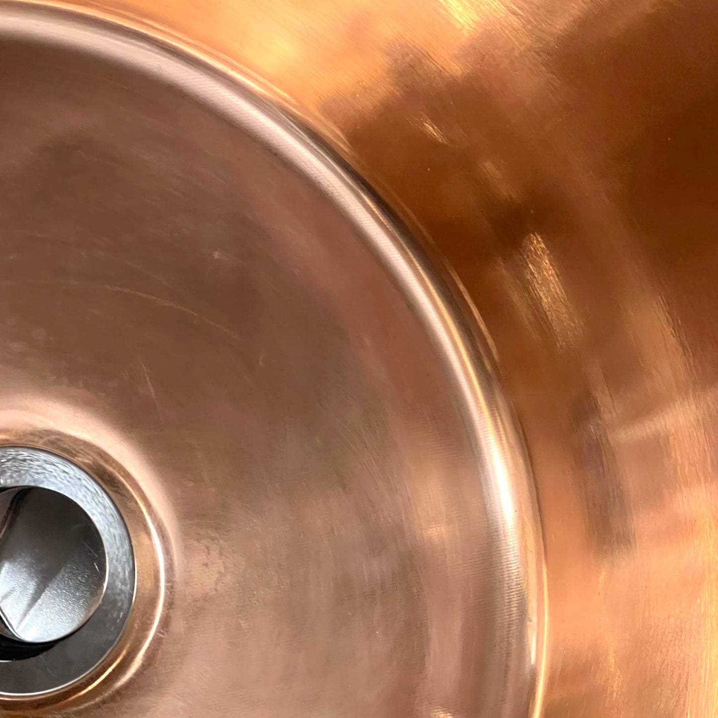 Close up of French copper bowl upcycled into a copper sink with iron handles and a chrome pop up waste on a white background