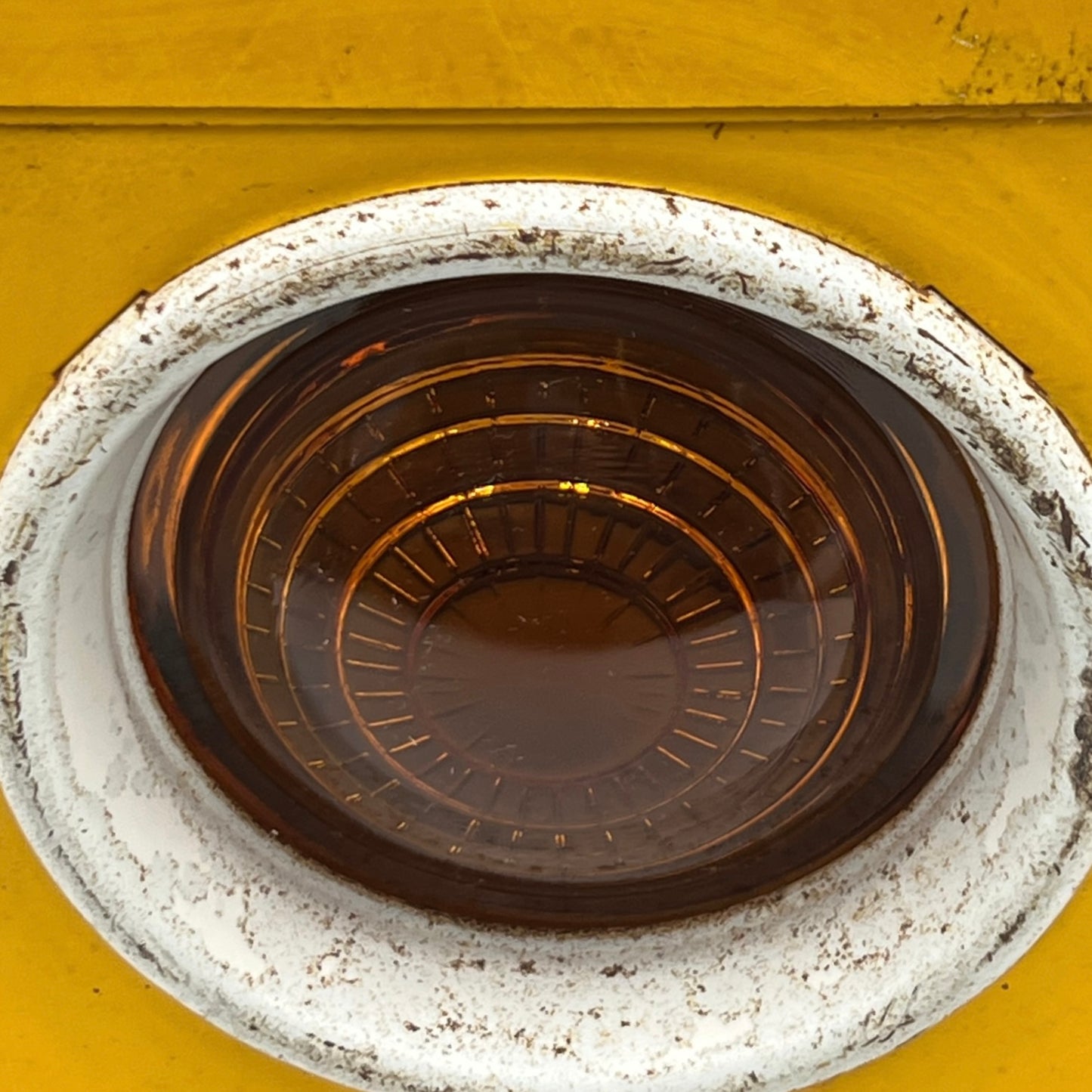 Close up of yellow vintage railway or railroad lamp with orange glass panels and a hook on a white background