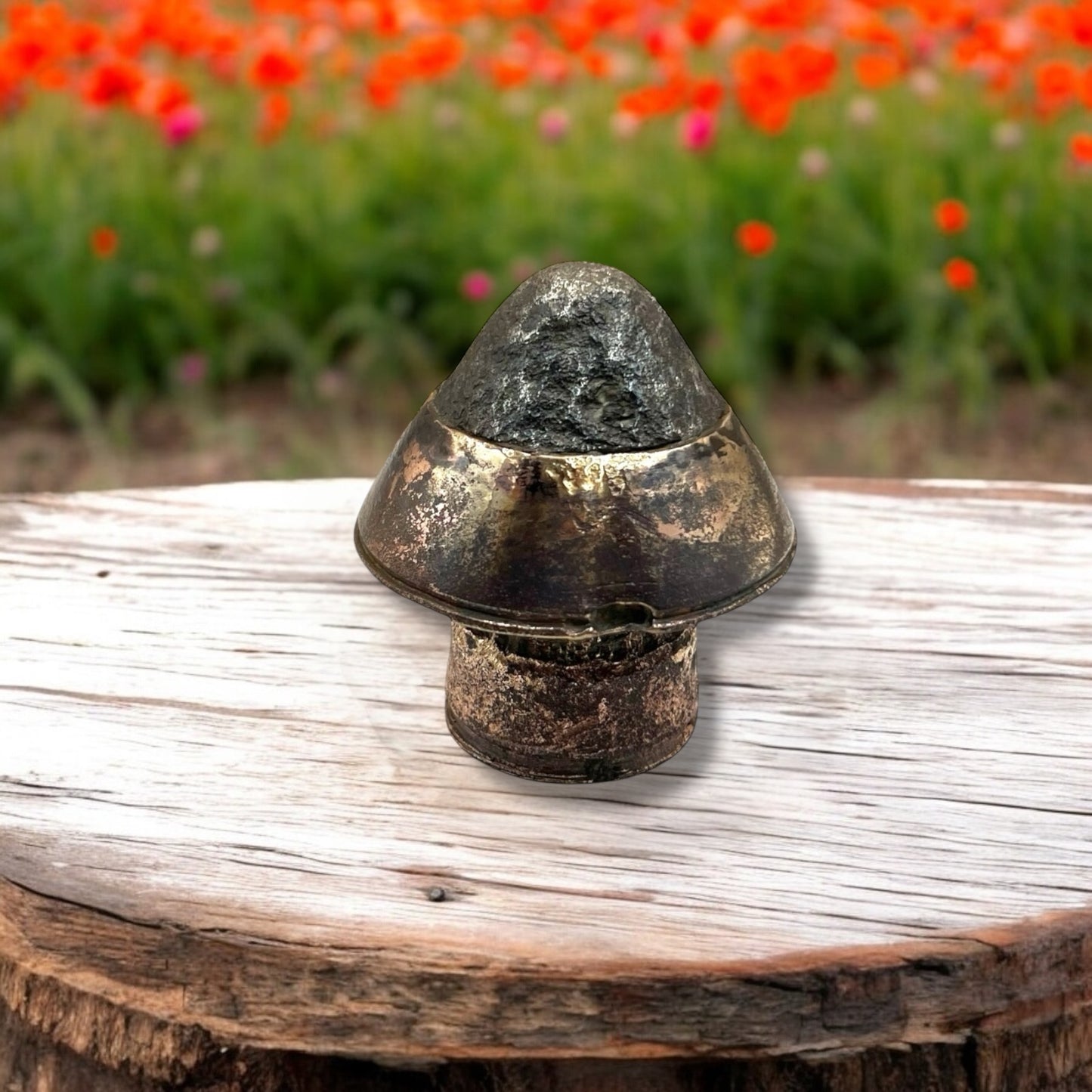 German WW1 brass and steel inert fuse paperweight in a well used relic condition on a wooden table in a field of poppies