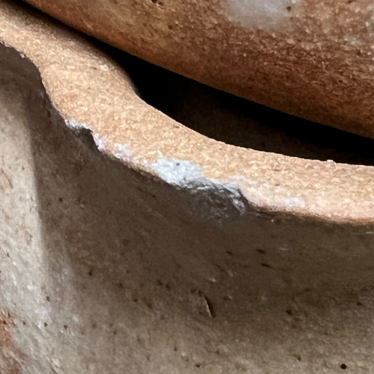 Close-up detail of a handmade terracotta clay vessel showing the textured, earthy brown surface and a white painted rim accent.