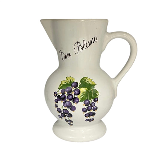 A white ceramic pitcher with a handle, featuring a hand-painted illustration of purple grapes and green leaves on the front, with 'Vin Blanc' written in black script on the side.