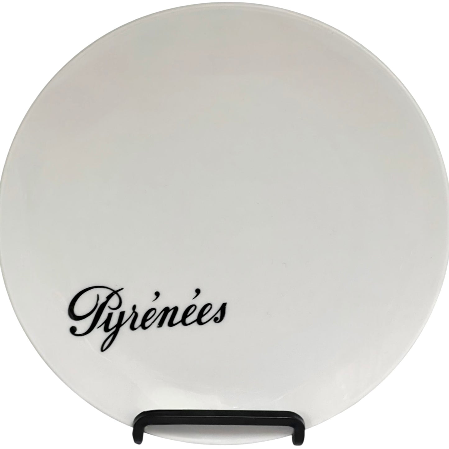 Round white plate with 'Pyrénèes' text on a stand against a white background