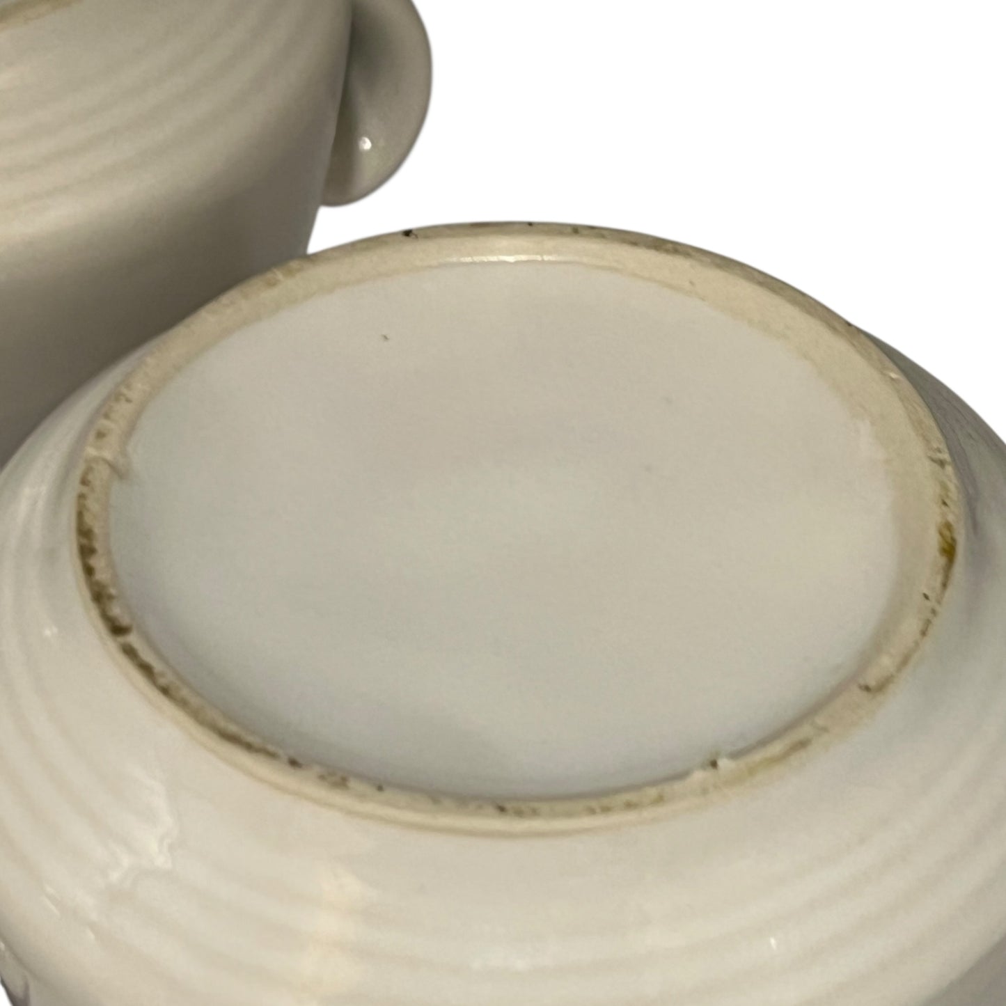 lose-up of a ceramic bowl base with a smooth, light-coloured glaze on a white background
