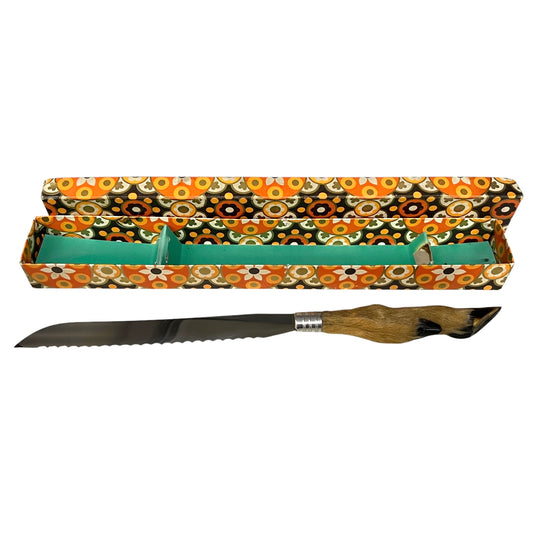 A serrated bread knife with a brown animal-hide handle and silver bolster, displayed horizontally next to its open patterned storage box on a white background.
