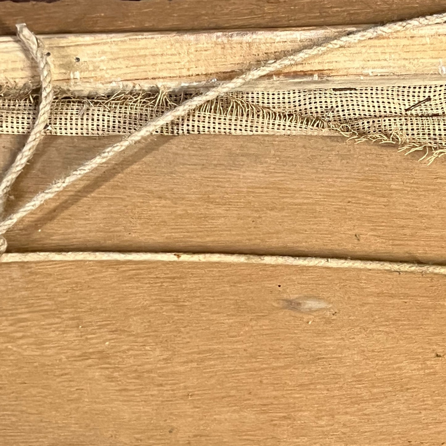Close-up of a natural jute rope wrapped around a light brown wooden surface, with a strip of beige burlap fabric visible along the top.