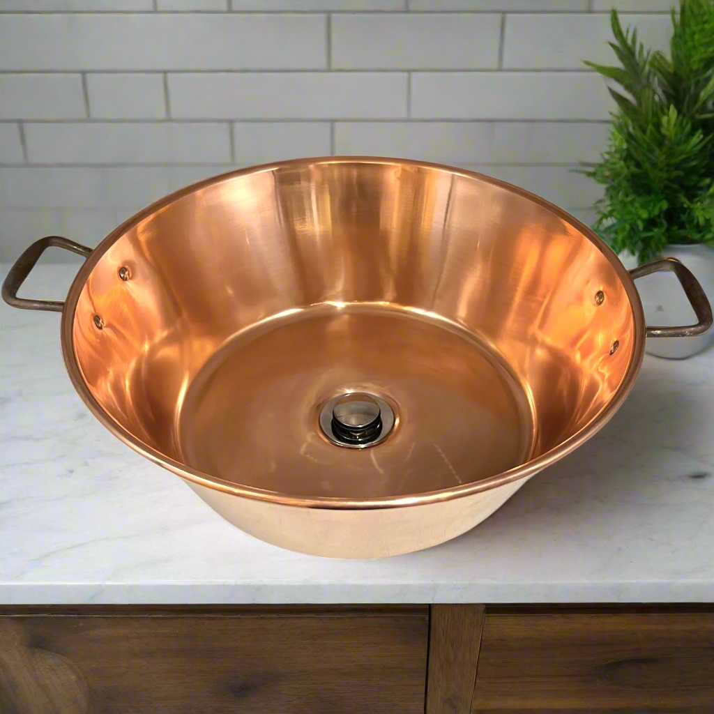 French copper bowl upcycled into a copper sink with iron handles and a chrome pop up waste on a vanity unit in a bathroom with a plant in the background