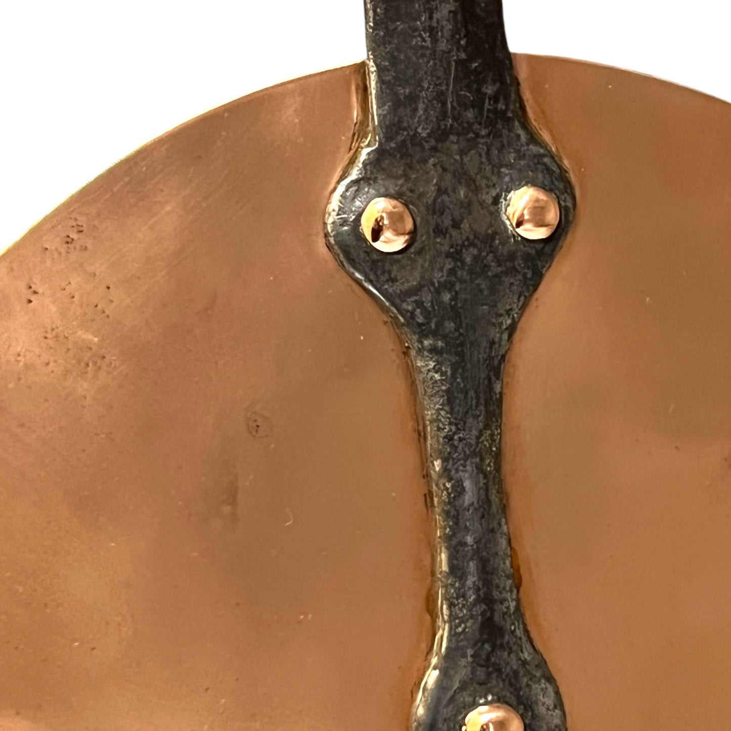 Close-up of a black cast iron metal handle of a copper pan lid on a white background