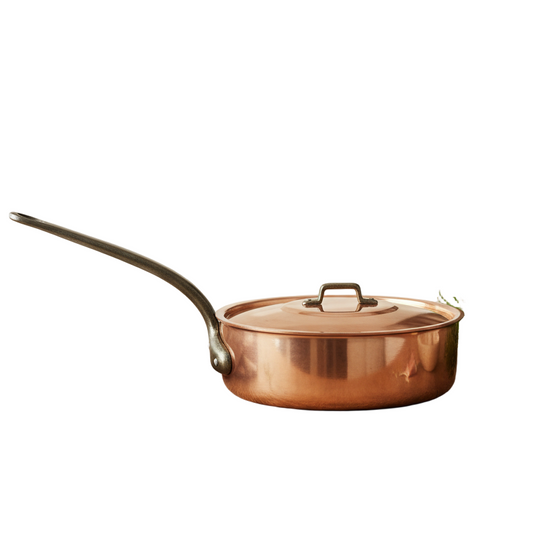 Copper pot on a wooden surface with a kitchen setting in the background