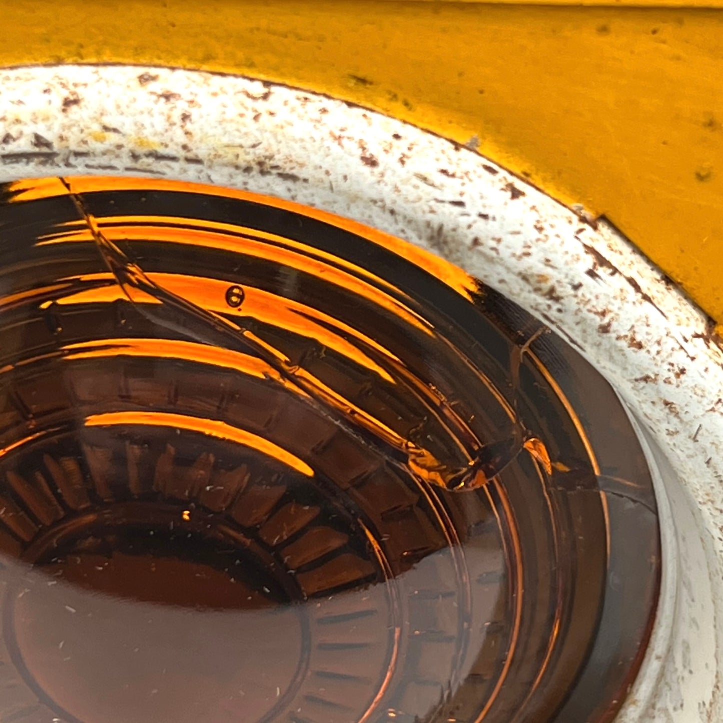 Close up of yellow vintage railway or railroad lamp with orange glass panels and a hook on a white background