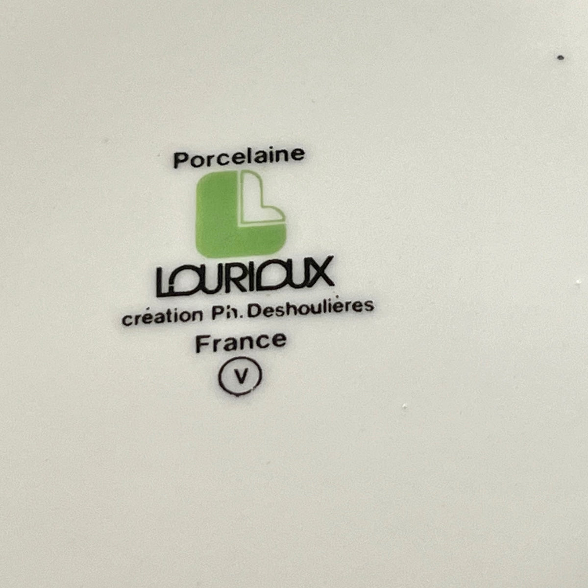 A close-up of a white porcelain surface printed with the brand name 'LOURIDUX', 'France', and a green monogram logo.
