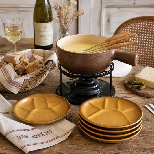 Fondue setup with brown fondue pot, plates, bread, a plate set and wine on a wooden table.