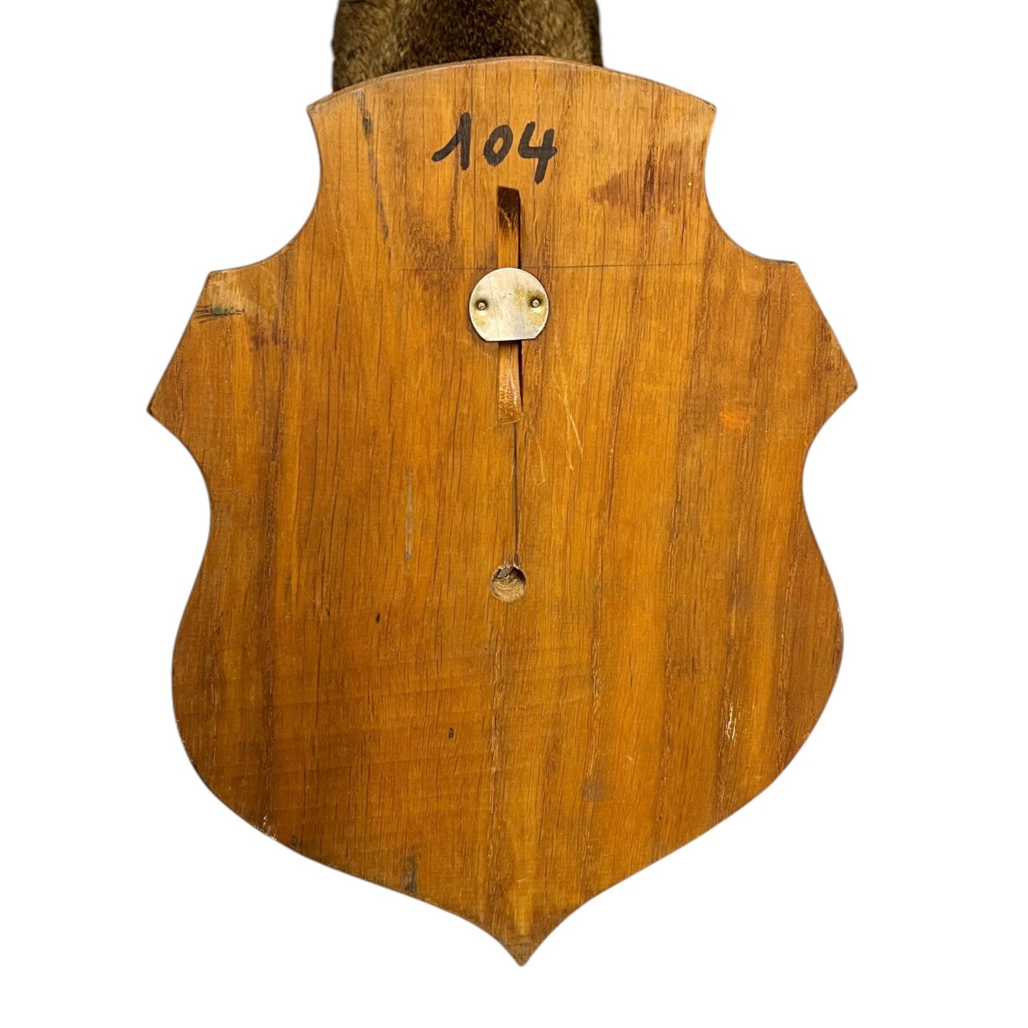 A close-up of a shield-shaped wooden wall plaque or cabinet backplate, showing a warm honey-brown wood grain finish, a brass hanging loop, and the handwritten number '104' at the top, set against a plain white background.