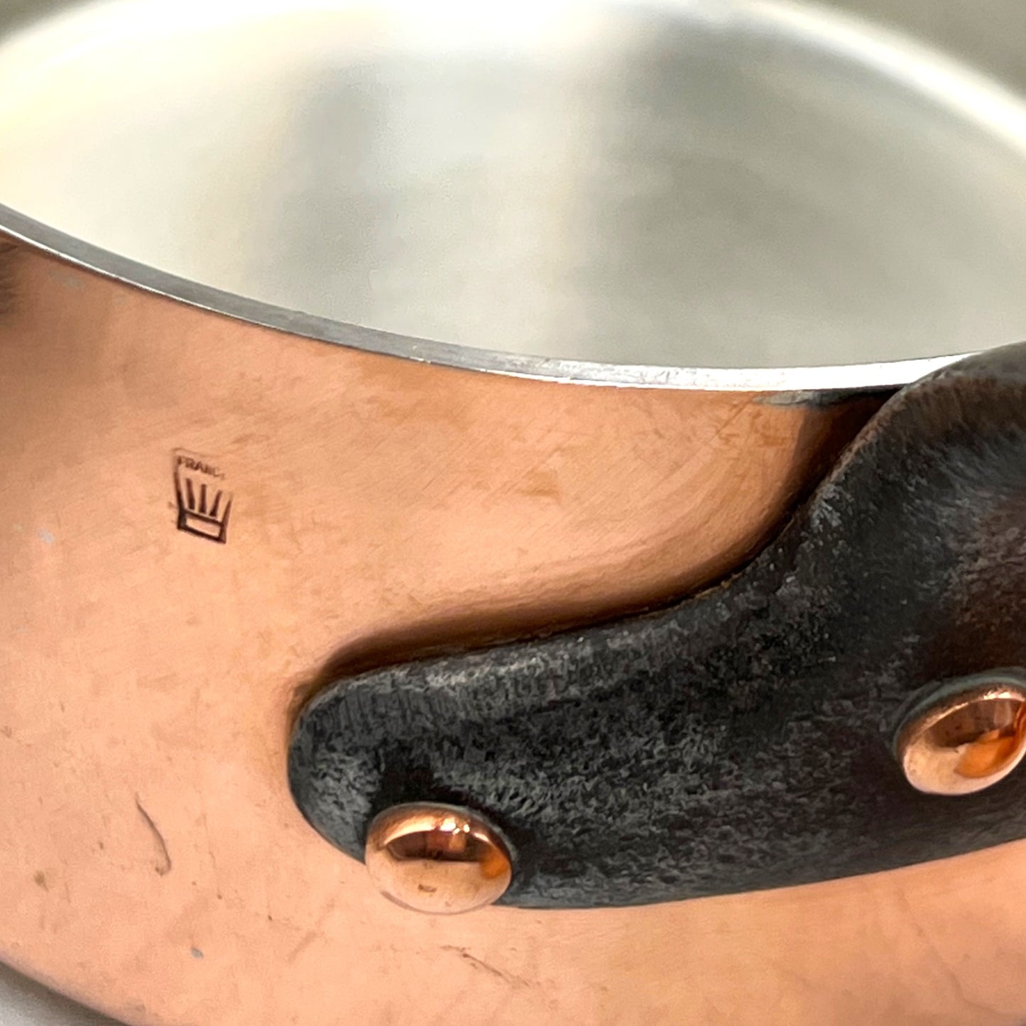 Close-up of a copper pot with a black handle and visible brand logo.