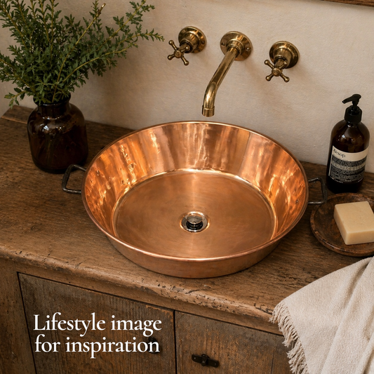 Copper sink on a wooden countertop with gold faucet and decorative elements.