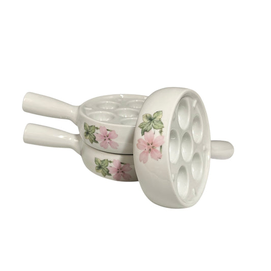 Three white porcelain escargot plates with pink floral designs, arranged on a plain white background