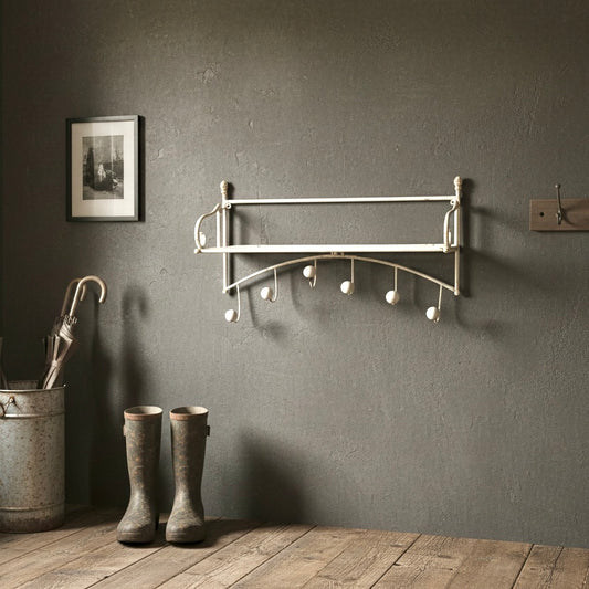 Wall-mounted coat rack with hooks on a gray wall, next to boots and an umbrella.