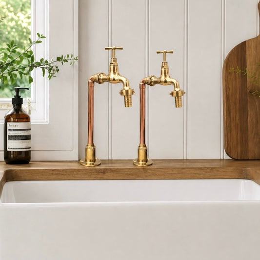 A pair of gold faucets sit on a wooden countertop beside a white sink.