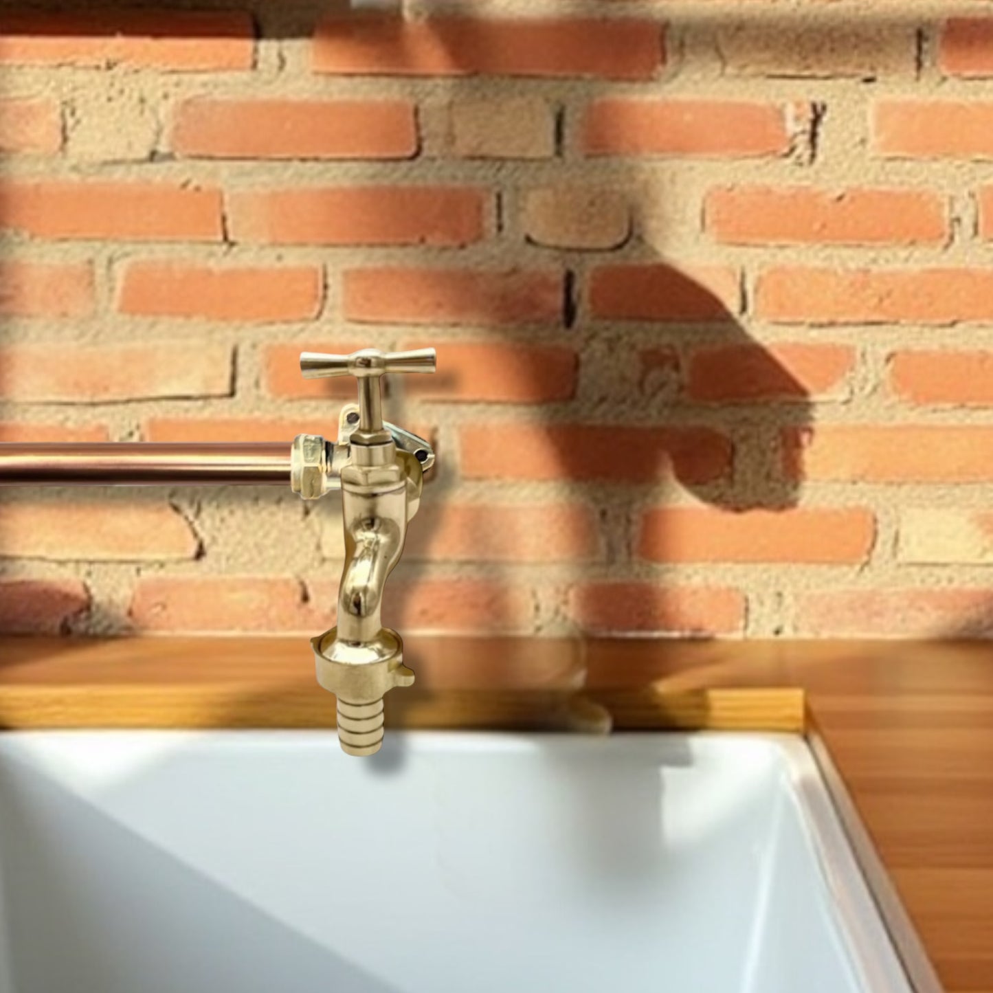 Brass faucet tap on a white sink against a brick wall