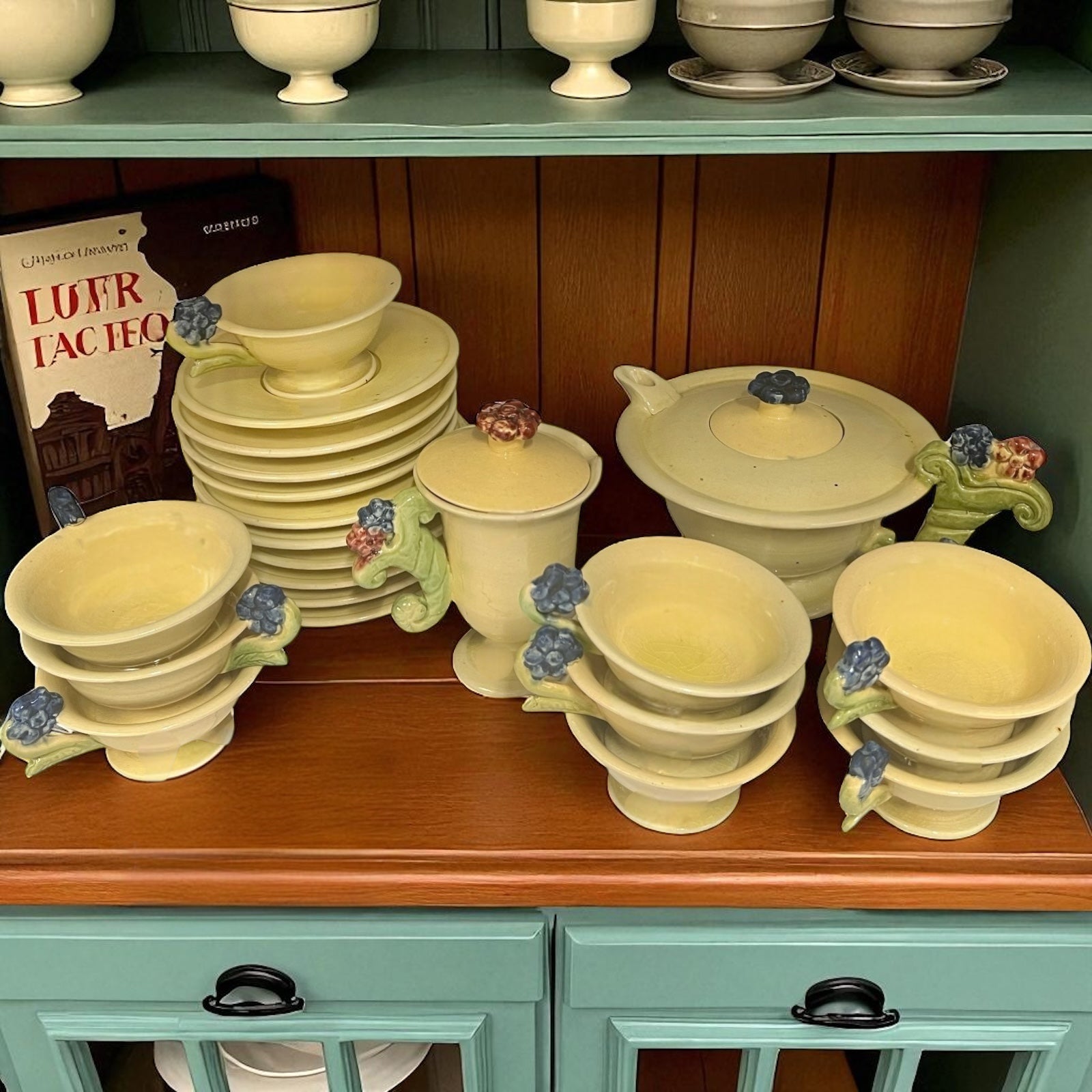 Collection of ceramic tea set on a wooden shelf with a green cabinet below.