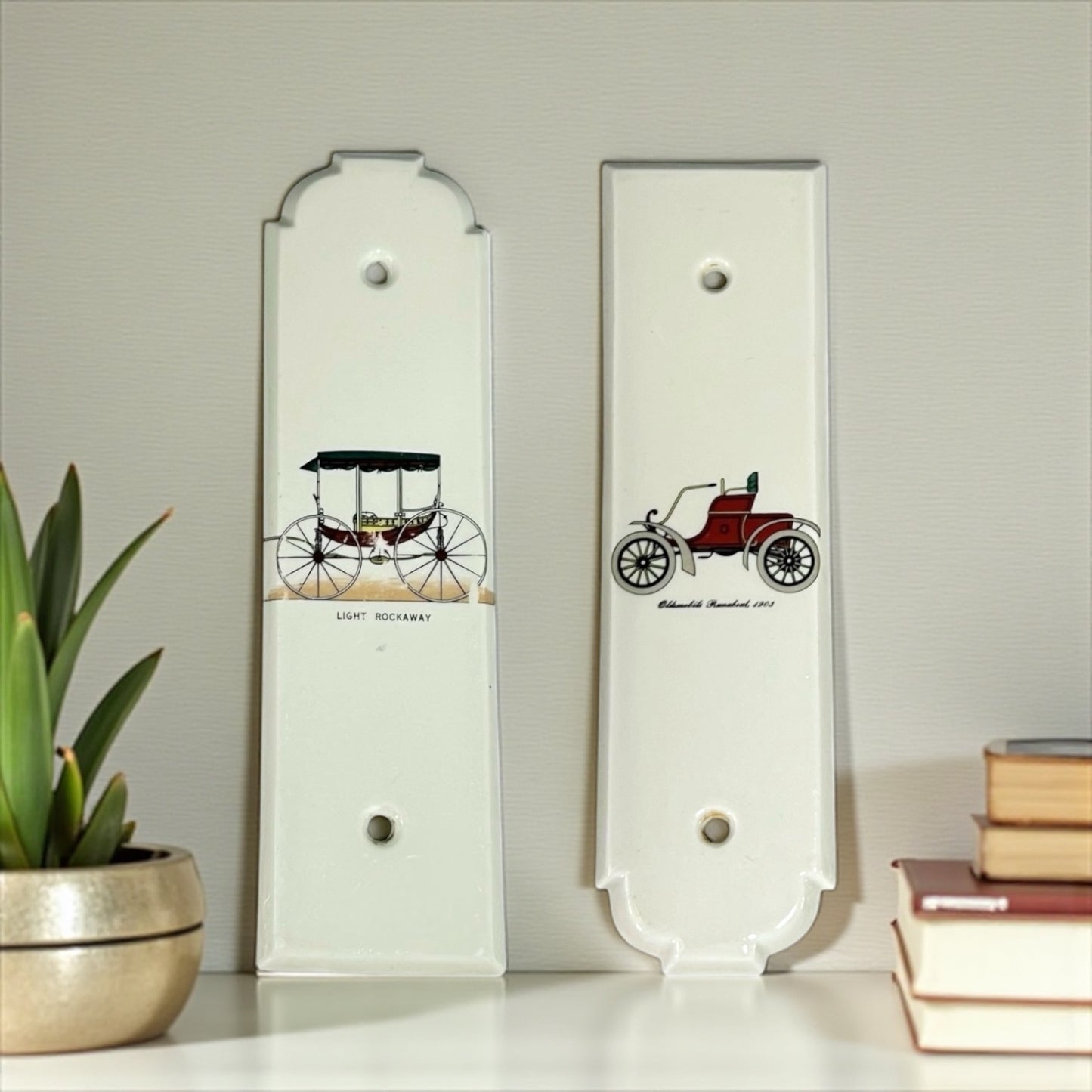 Two decorative porcelain door push plates with vintage car illustrations on a light grey background.