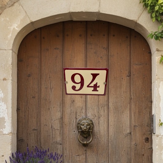 Wooden door with a house number plaque and lion knocker on a stone building.