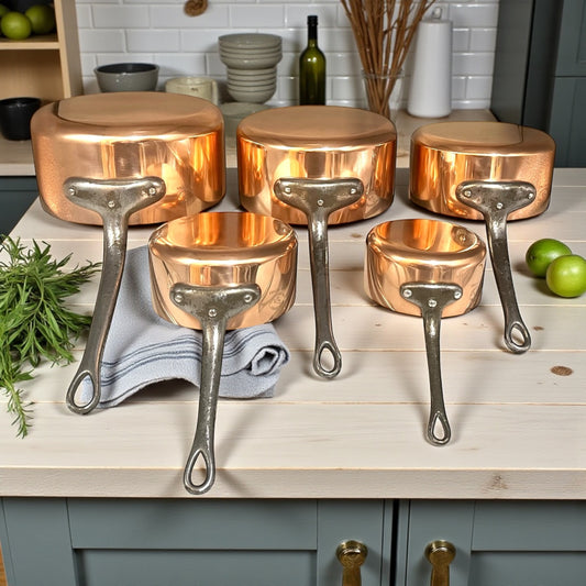 Set of copper cookware with grey handles on a kitchen counter.