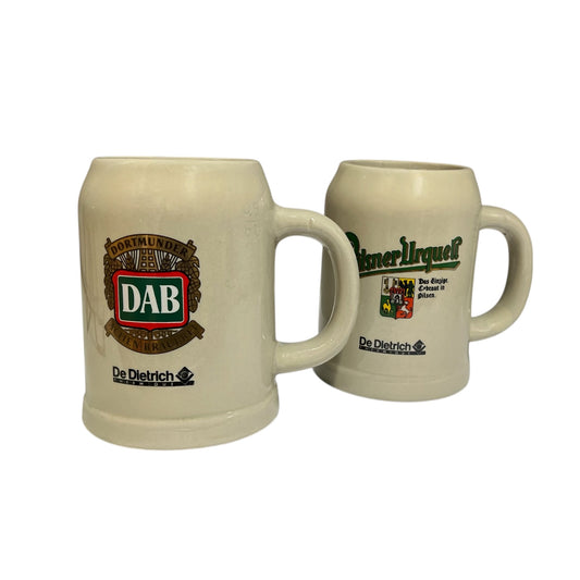 Two cream-colored ceramic beer steins with printed De Dietrich and DAB logos, shown on a plain white background.