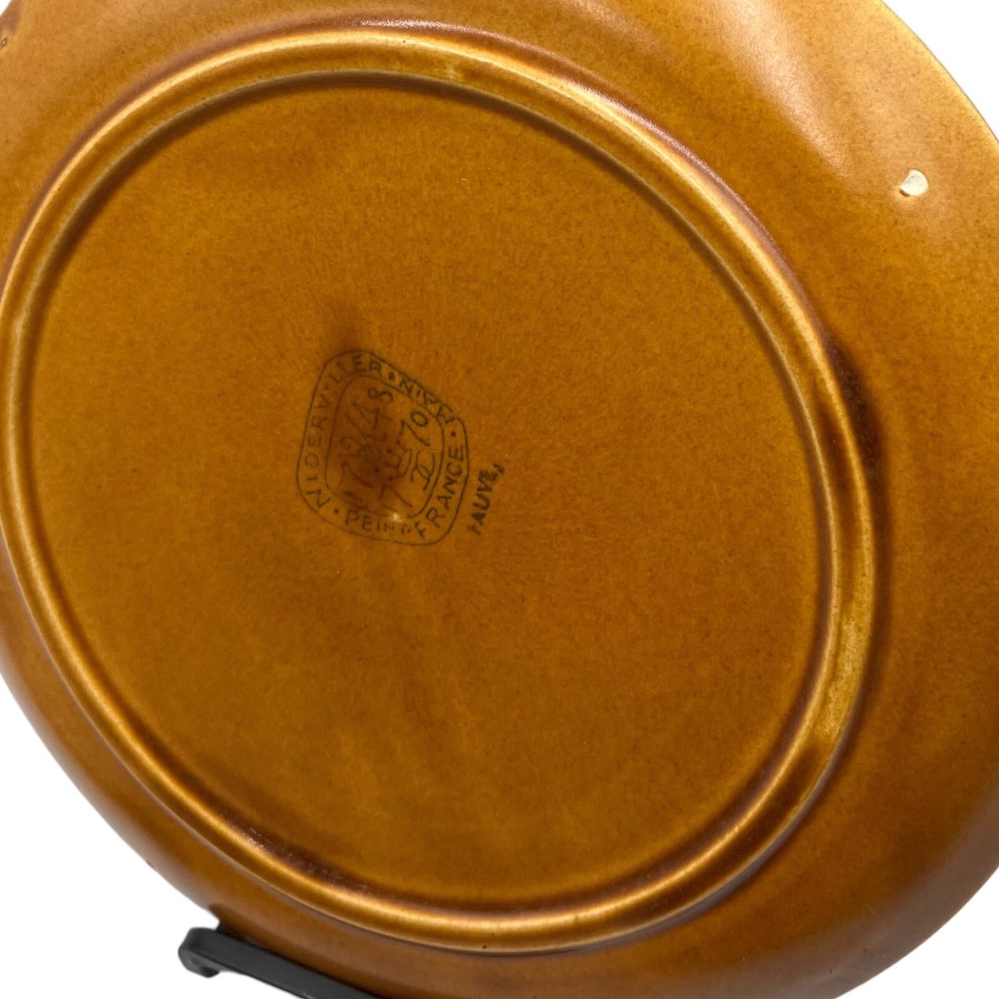 Reverse side of a single amber and white speckled fondue plate made by Niderviller with 6 raised sections showing the makers print on the reverse on a white background