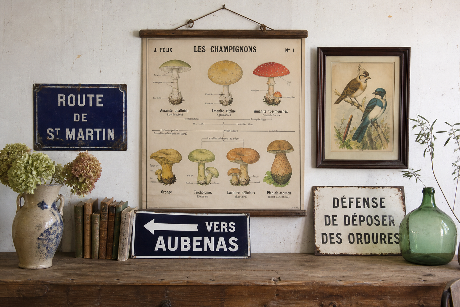 A vignette scene of a hanging vintage French poster, a French enamel road sign and a direction sign, on a wooden top with 2 vases and flowers forming a vintage aesthetic display for a collection including road signs, posters and wooden pictures
