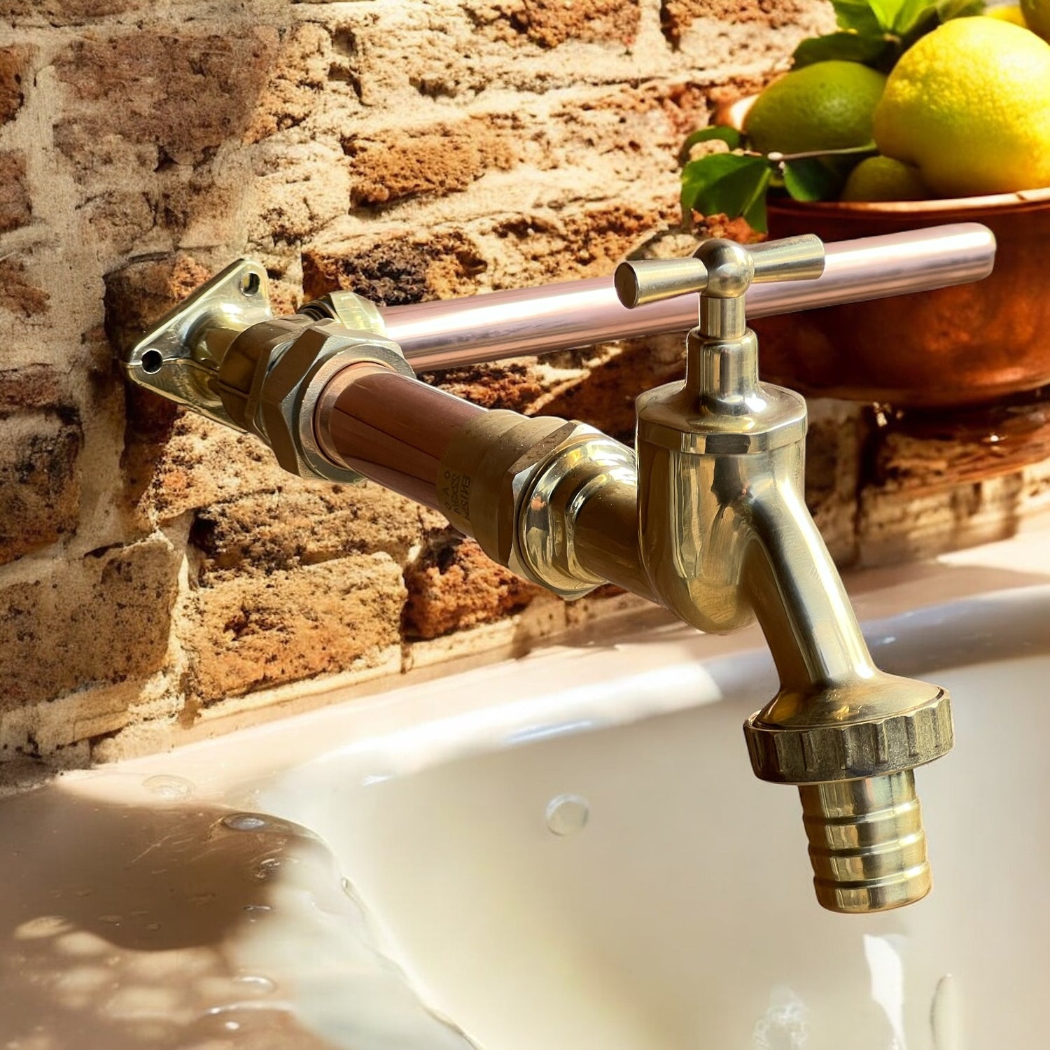 Brass tap with a nozzle and copper pipework fitted on a brick wall in a rustic kitchen over a white pot sink