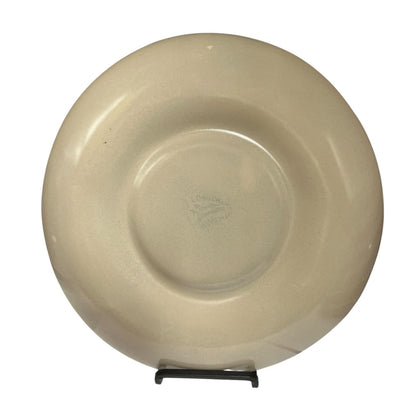 A round ceramic plate in a warm cream or light beige color, displayed upright on a small black stand against a plain white background.