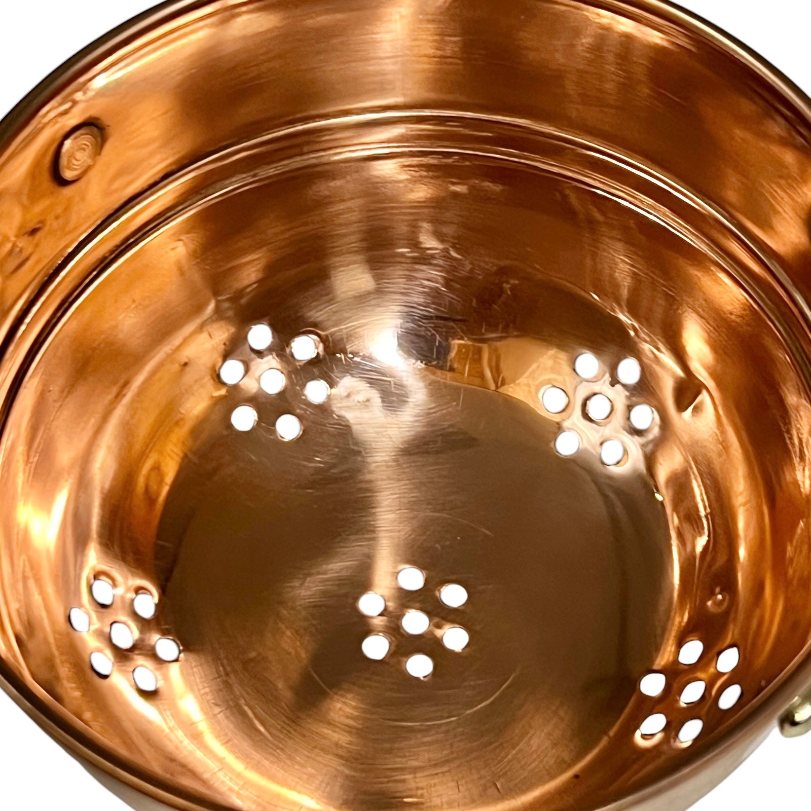 Close-up of the interior of a copper sieve or pan, showing a shiny metallic copper surface with several circular drainage holes near the bottom.