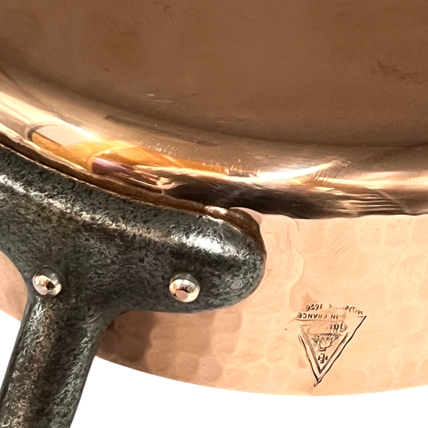 Close-up of a copper pot with a black handle and a visible brand logo.