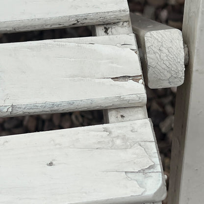 A close-up view of a painted wooden slatted garden chair set amidst a lush garden backdrop.