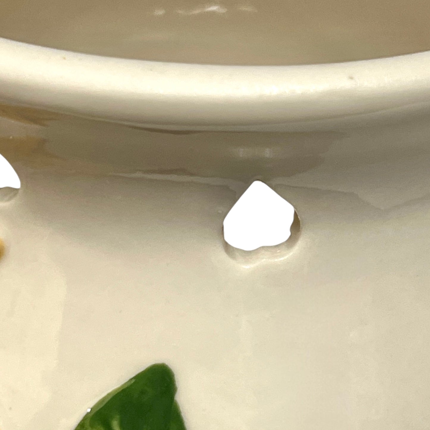 Close-up of a white ceramic onion jar with a small hole and green leaves.