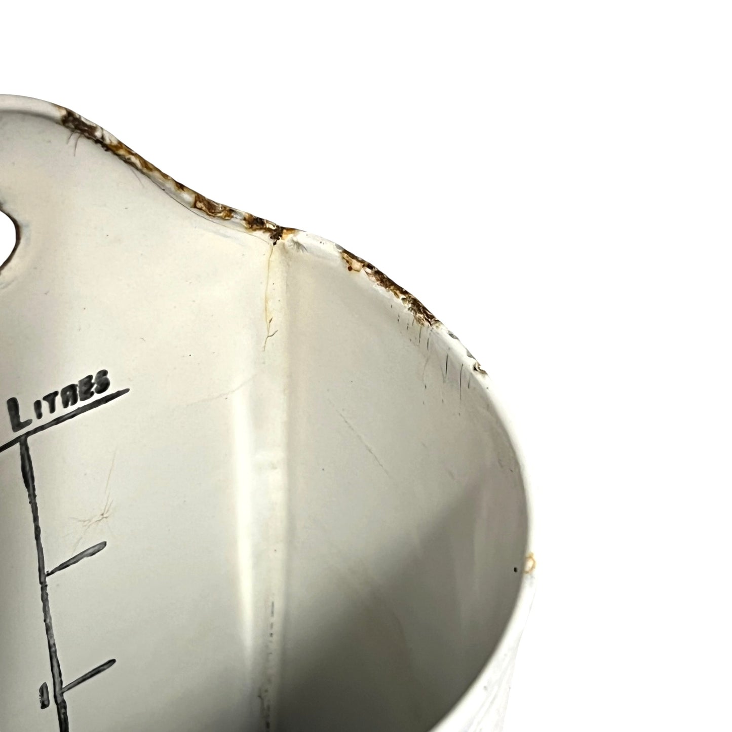 Close-up of the interior of a white metal measuring container with printed litre markings and a worn, rusted rim against a white background.