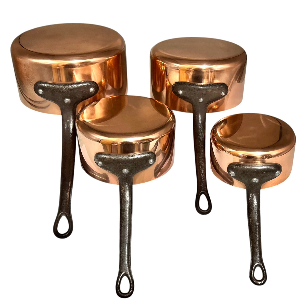 Four copper saucepans with dark cast iron handles, arranged on a plain white background.