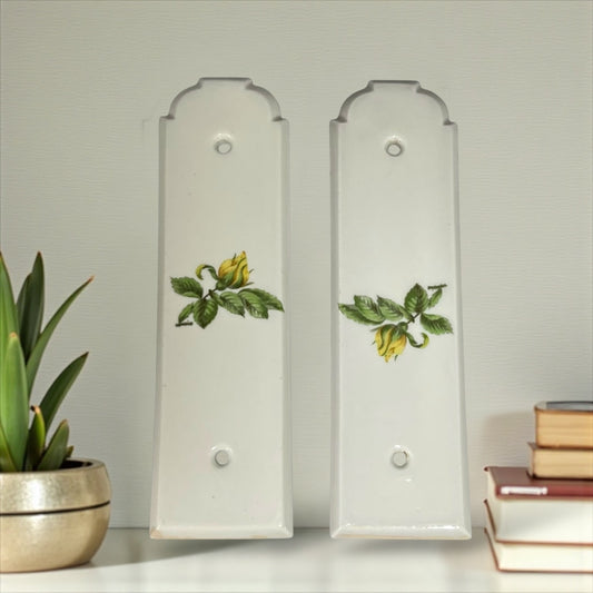 Two white finger push door plates with floral designs on a light grey background for sale from All Things French Store
