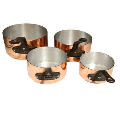Four copper saucepans with dark cast iron handles, arranged by size on a plain white background.