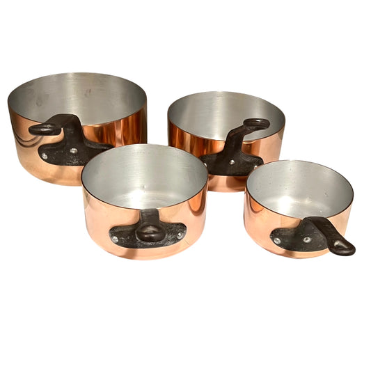 Four copper saucepans with dark cast iron handles, arranged by size on a plain white background.