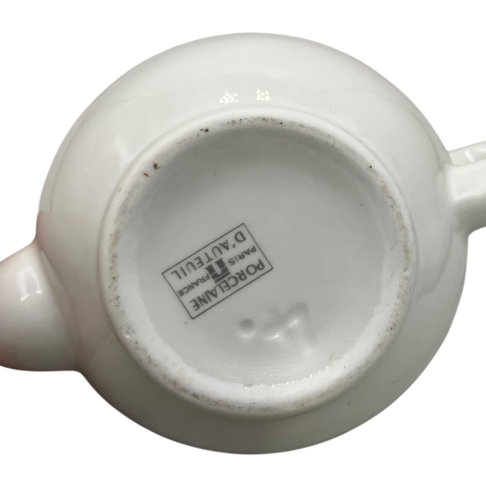 Close-up of a white ceramic teapot with a visible brand label on a white background