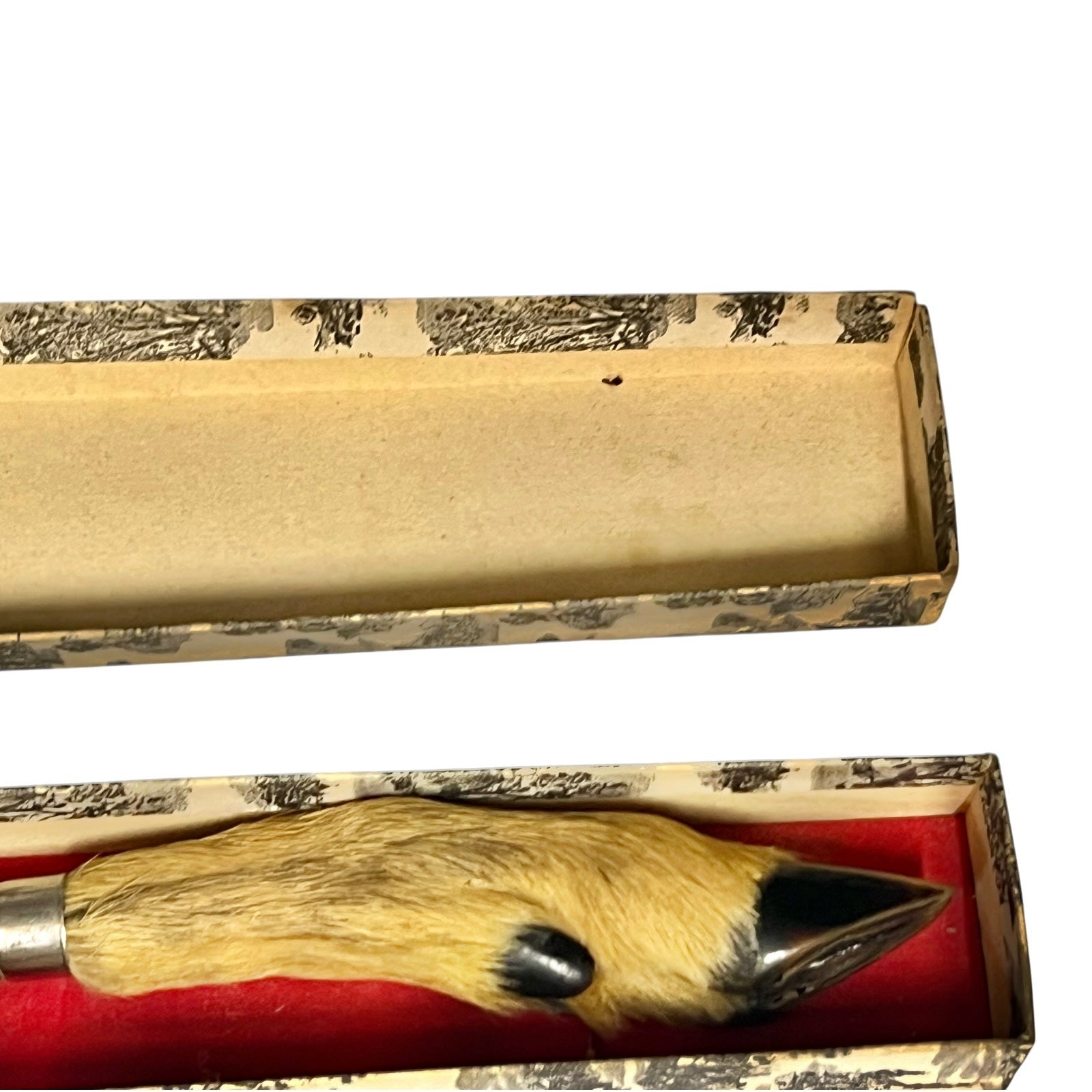 A vintage decorative knife with a deer hoof handle, displayed inside its open patterned presentation box with a red velvet lining.
