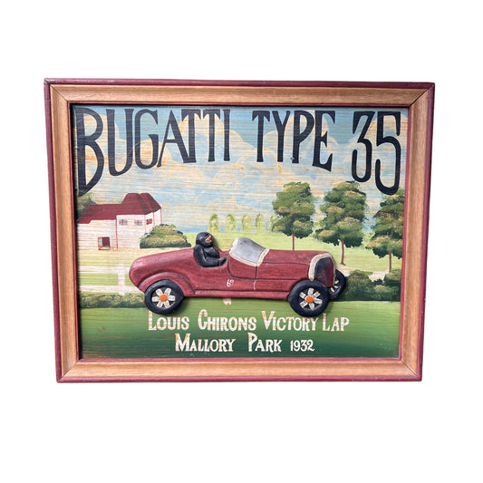 A framed vintage-style decorative sign featuring a painted Bugatti Type 35 race car on a green field with trees and a house in the background. Large text reads “BUGATTI TYPE 35,” with smaller text below reading “Louis Chirons Victory Lap Mallory Park 1932.