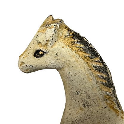 A close-up of a horse head sculpture in profile, featuring a textured off-white surface with distressed black and warm tan detailing along the mane and head.